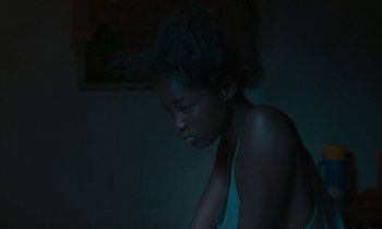 Movie still from “Atlantics” (2019), directed by Mati Diop – A woman sitting in a dark room with her hair blowing in the wind; Close Up shot, High angle