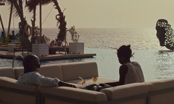 Movie still from “Atlantics” (2019), directed by Mati Diop – A man and a woman sitting on a couch next to the ocean; Wide shot, High angle