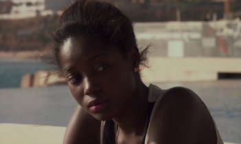 Movie still from “Atlantics” (2019), directed by Mati Diop – A young woman sitting on the side of the road; Close Up shot, Over the shoulder angle