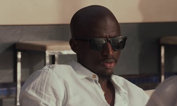 Movie still from “Atlantics” (2019), directed by Mati Diop – A man wearing sunglasses and a white shirt; Close Up shot, Low angle