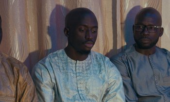 Movie still from “Atlantics” (2019), directed by Mati Diop – A man in a blue and white shirt is looking down; Medium shot, High angle