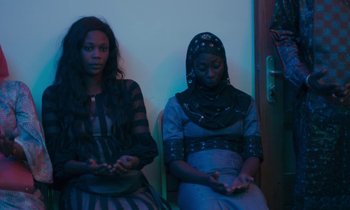 Movie still from “Atlantics” (2019), directed by Mati Diop – Two women sitting on a bench in a room; Medium shot, High angle