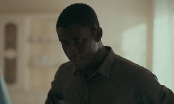 Movie still from “Atlantics” (2019), directed by Mati Diop – A man in a brown shirt is looking at the camera; Close Up shot, Low angle