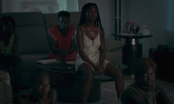 Movie still from “Atlantics” (2019), directed by Mati Diop – A woman sitting on top of a coffee table next to another woman; Medium shot, High angle