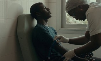 Movie still from “Atlantics” (2019), directed by Mati Diop – A man sitting in front of another man in a room; Medium shot, Low angle