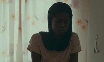 Movie still from “Atlantics” (2019), directed by Mati Diop – A young woman wearing a head scarf is looking down; Close Up shot, High angle