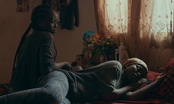 A man and a woman laying on a bed in front of a vase of flowers