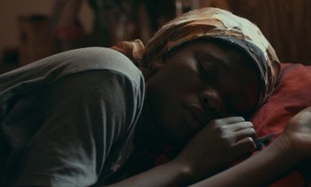 Movie still from “Atlantics” (2019), directed by Mati Diop – A person sleeping on a bed with a blanket on their head; Close Up shot, High angle