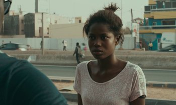 Movie still from “Atlantics” (2019), directed by Mati Diop – A woman standing on the side of a road; Close Up shot, Over the shoulder angle