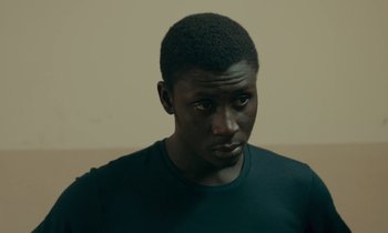 Movie still from “Atlantics” (2019), directed by Mati Diop – A person wearing a green shirt; Close Up shot, High angle