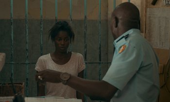 Movie still from “Atlantics” (2019), directed by Mati Diop – A woman standing in front of an officer holding a watch; Medium shot, Over the shoulder angle