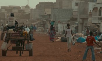 Movie still from “Atlantics” (2019), directed by Mati Diop – A group of people walking down a dirt road; Extreme Wide shot, Over the shoulder angle
