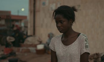 Movie still from “Atlantics” (2019), directed by Mati Diop – A young black woman looking down while standing in front of a wall; Close Up shot, Over the shoulder angle
