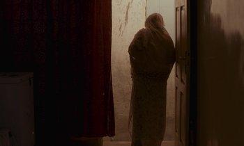 Movie still from “Atlantics” (2019), directed by Mati Diop – A person standing in front of an open door; Medium shot, Low angle