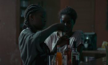 Movie still from “Atlantics” (2019), directed by Mati Diop – Two young women sitting at a table in front of drinks; Close Up shot, Over the shoulder angle