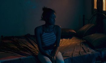 Movie still from “Atlantics” (2019), directed by Mati Diop – A woman sitting on top of a bed in a dark room; Medium shot, High angle