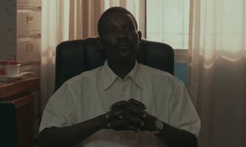 Movie still from “Atlantics” (2019), directed by Mati Diop – A man sitting in an office chair with his hands clasped together; Close Up shot, Low angle