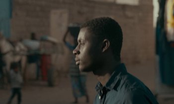 Movie still from “Atlantics” (2019), directed by Mati Diop – A young man is looking into the distance while standing in front of a brick wall; Close Up shot, Low angle