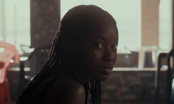 Movie still from “Atlantics” (2019), directed by Mati Diop – A woman with long braids is looking at the camera; Close Up shot, Over the shoulder angle