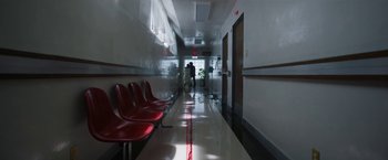 Movie still from “Bardo: False Chronicle of a Handful of Truths” (2022), directed by Alejandro G. Iñárritu – A long hallway with red chairs and a person walking in the distance; Extreme Wide shot, High angle