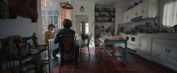 Movie still from “Bardo: False Chronicle of a Handful of Truths” (2022), directed by Alejandro G. Iñárritu – Two people are sitting at a table in a kitchen; Wide shot, High angle