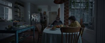 Movie still from “Bardo: False Chronicle of a Handful of Truths” (2022), directed by Alejandro G. Iñárritu – Two people sitting at a dining room table with a laptop computer; Wide shot, Low angle