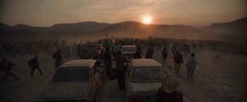 Movie still from “Bardo: False Chronicle of a Handful of Truths” (2022), directed by Alejandro G. Iñárritu – A group of people standing next to cars on a dirt road; Extreme Wide shot, High angle