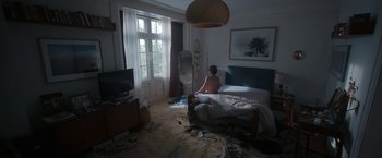 Movie still from “Bardo: False Chronicle of a Handful of Truths” (2022), directed by Alejandro G. Iñárritu – A person sitting on a bed in a room; Wide shot, High angle