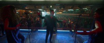 Movie still from “Bardo: False Chronicle of a Handful of Truths” (2022), directed by Alejandro G. Iñárritu – A man in a black suit and red gloves on a stage; Wide shot, Low angle