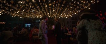 Movie still from “Bardo: False Chronicle of a Handful of Truths” (2022), directed by Alejandro G. Iñárritu – Two men are talking in a room with lights overhead; Wide shot, Low angle