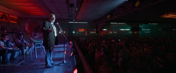 Movie still from “Bardo: False Chronicle of a Handful of Truths” (2022), directed by Alejandro G. Iñárritu – A man standing on a stage in front of a crowd; Wide shot, Over the shoulder angle