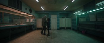Movie still from “Bardo: False Chronicle of a Handful of Truths” (2022), directed by Alejandro G. Iñárritu – Two people are standing in a room in front of a row of toilets; Wide shot, High angle