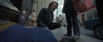 Movie still from “Bardo: False Chronicle of a Handful of Truths” (2022), directed by Alejandro G. Iñárritu – An older man sitting on the ground on the sidewalk; Medium shot, Low angle