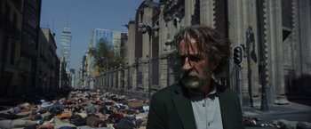 Movie still from “Bardo: False Chronicle of a Handful of Truths” (2022), directed by Alejandro G. Iñárritu – A man standing in front of a group of people laying on the ground in front of a building; Medium shot, Low angle