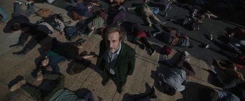 Movie still from “Bardo: False Chronicle of a Handful of Truths” (2022), directed by Alejandro G. Iñárritu – A group of people laying on the ground and a man in a green suit; Wide shot, High angle