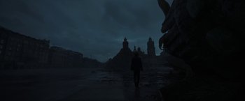 Movie still from “Bardo: False Chronicle of a Handful of Truths” (2022), directed by Alejandro G. Iñárritu – A person walking in the rain near a large building; Extreme Wide shot, Low angle