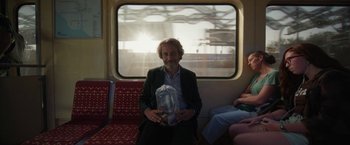 Movie still from “Bardo: False Chronicle of a Handful of Truths” (2022), directed by Alejandro G. Iñárritu – A man sitting on a train holding a water bottle; Medium shot, Low angle