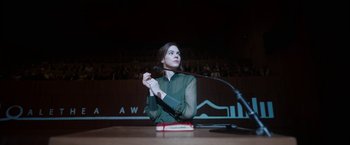 Movie still from “Bardo: False Chronicle of a Handful of Truths” (2022), directed by Alejandro G. Iñárritu – A woman sitting in front of a microphone in front of an audience; Medium shot, Low angle