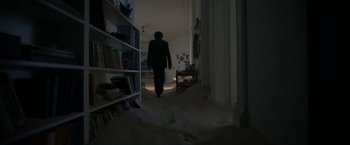 Movie still from “Bardo: False Chronicle of a Handful of Truths” (2022), directed by Alejandro G. Iñárritu – A person walking in a room with a book shelf; Wide shot, High angle