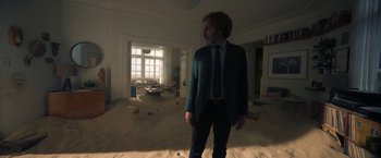 Movie still from “Bardo: False Chronicle of a Handful of Truths” (2022), directed by Alejandro G. Iñárritu – A man in a suit and tie standing in a living room; Wide shot, High angle
