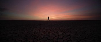 Movie still from “Bardo: False Chronicle of a Handful of Truths” (2022), directed by Alejandro G. Iñárritu – A person walking across a dry ground at sunset; Extreme Wide shot, Low angle
