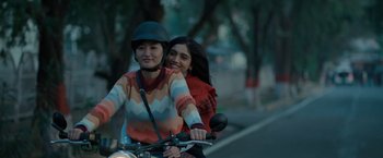 Two women riding a motorcycle down a street