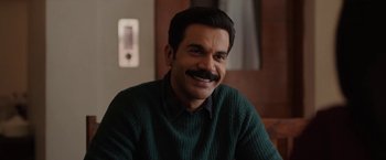 A man wearing a green sweater with a mustache