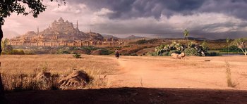 A dirt road leading to a city on a cloudy day