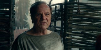 Movie still from “Barbarians” (2020), created by Arne Nolting – An older man is standing in front of a wooden structure; Close Up shot, Over the shoulder angle