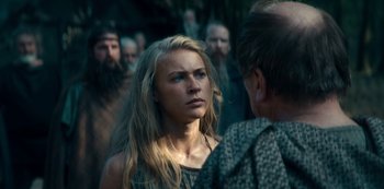 Movie still from “Barbarians” (2020), created by Arne Nolting – A woman with long blonde hair standing in front of a group of men; Close Up shot, Over the shoulder angle