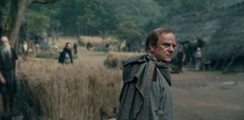 Movie still from “Barbarians” (2020), created by Arne Nolting – A man with a scarf on his head is standing in a field; Medium shot, Low angle