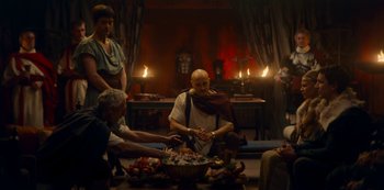 Movie still from “Barbarians” (2020), created by Arne Nolting – A group of people gathered around a bowl of fruit; Wide shot, Over the shoulder angle