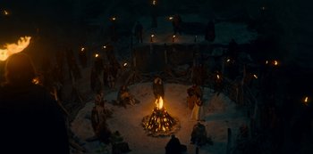 Movie still from “Barbarians” (2020), created by Arne Nolting – A group of people sitting around a fire in the snow; Extreme Wide shot, High angle