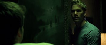 Movie still from “Joy Ride” (2001), directed by John Dahl – A man standing in front of a painting of boats; Medium shot, Over the shoulder angle